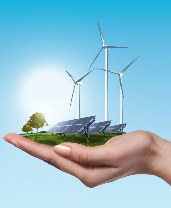 Wind turbines and solar panels on meadow with tree holds in womans hand against blue sky and clouds. Green energy concept